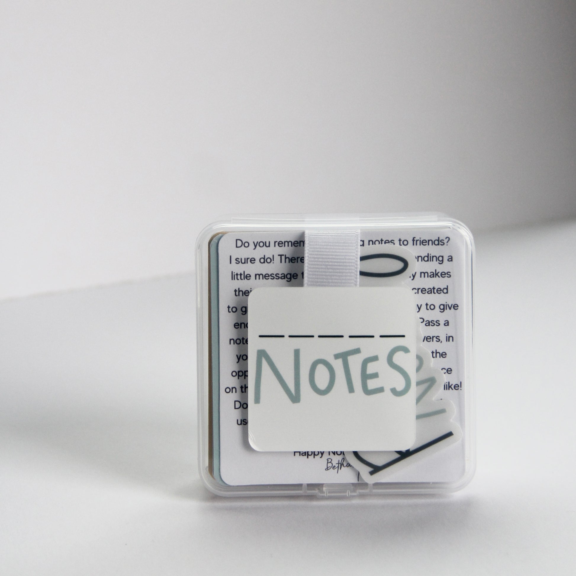 A small clear plastic case with a white square label reading "Fill in the Blank Notes" in a playful font. The box contains 40 durable note cards that include encouraging  prompts that you can fill out and pass on to others for a boost of  appreciation and encouragement!
