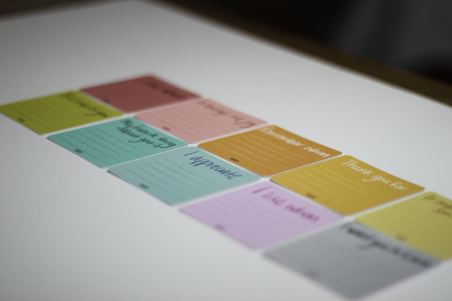 Colorful note cards placed on a surface, each with handwritten prompts like "Thank you for" and "I appreciate." These encouraging notes are arranged in two rows, featuring pastel shades of yellow, pink, blue, green, and purple.