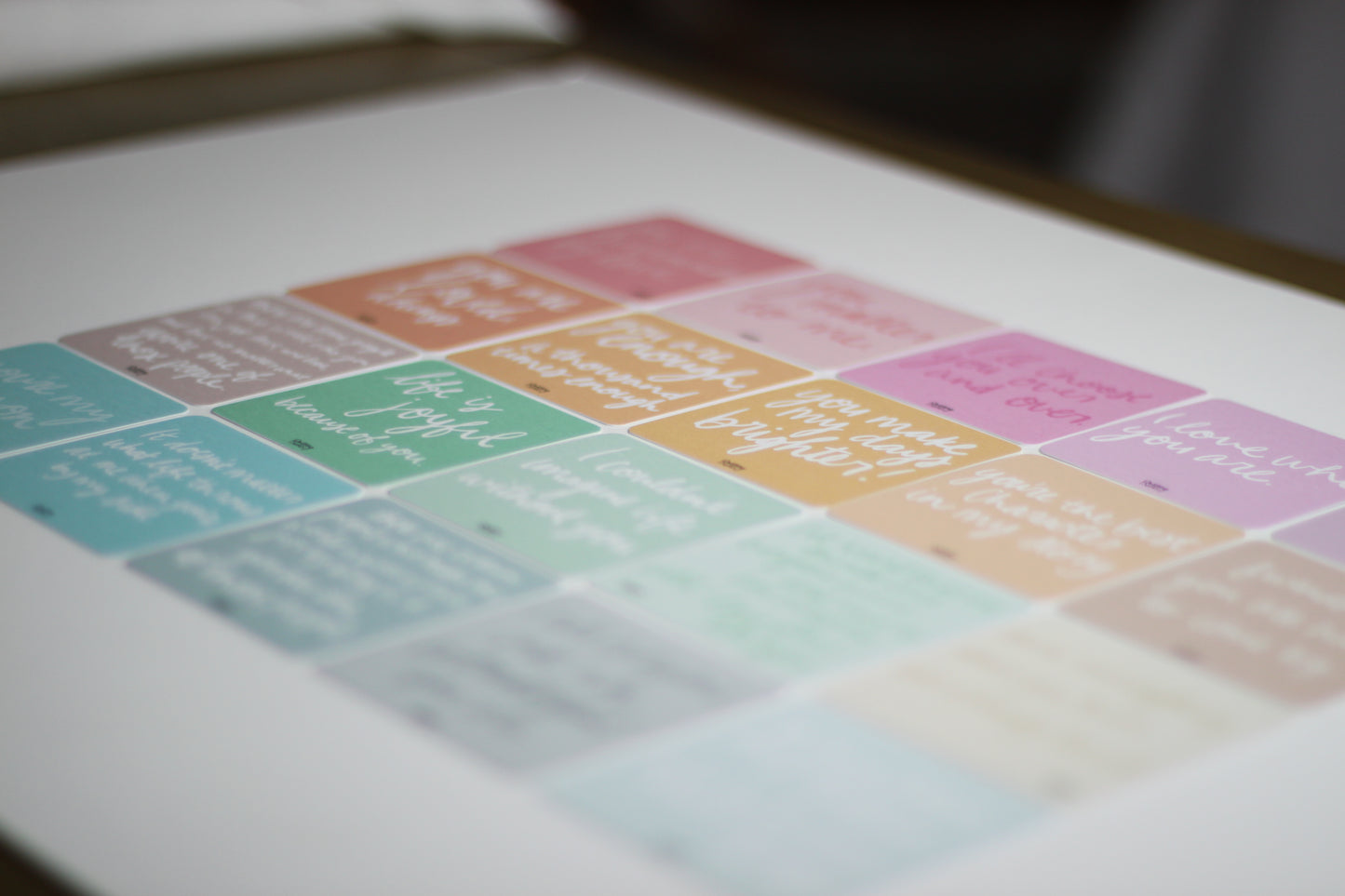 A blurred close-up image of pastel-colored love note cards. Each note card has handwritten motivational quotes, though the text remains unreadable. The peach, pink, purple, teal, and blue colors evoke the warmth of romantic relationships.