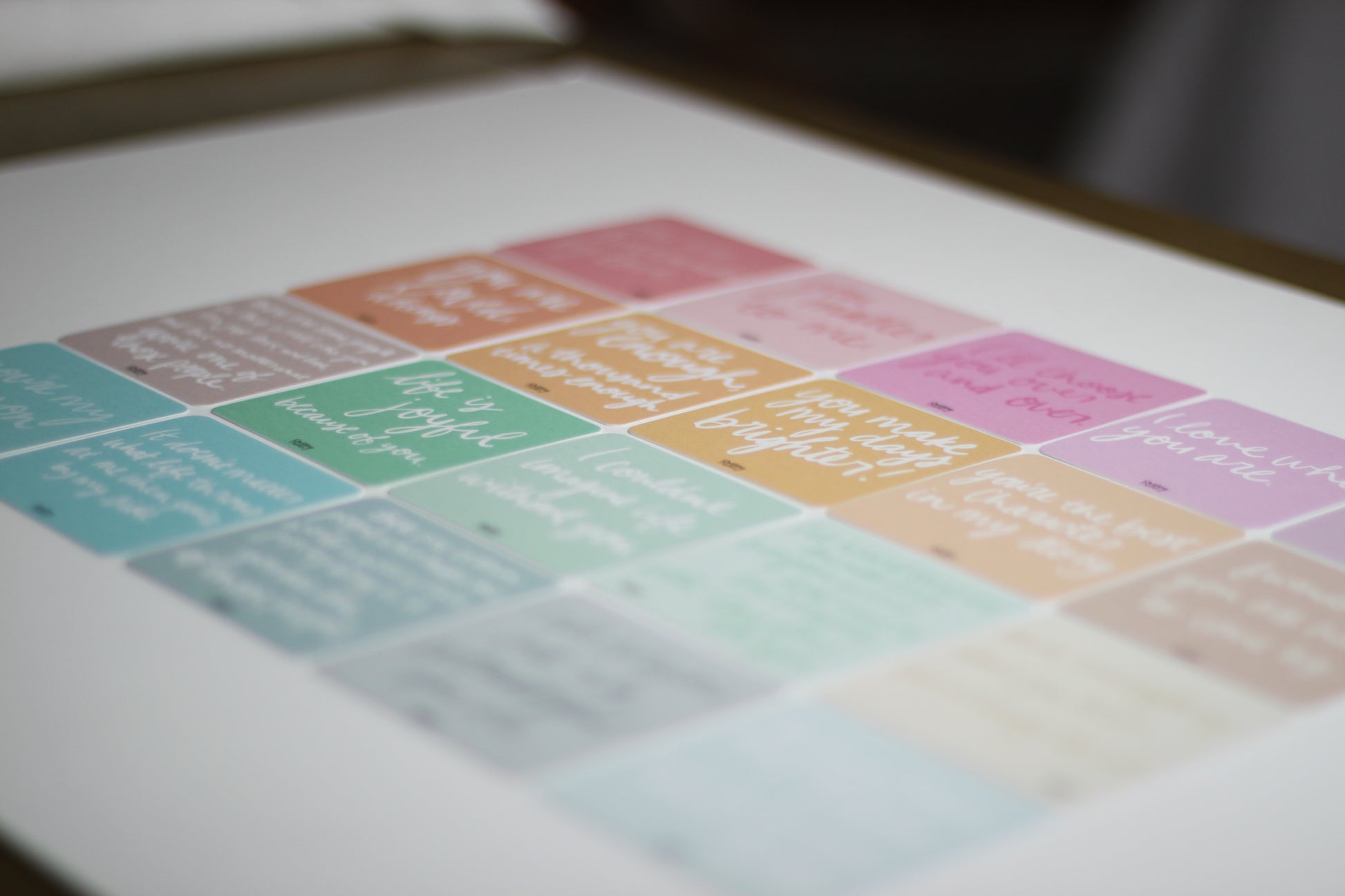 A blurred close-up image of pastel-colored love note cards. Each note card has handwritten motivational quotes, though the text remains unreadable. The peach, pink, purple, teal, and blue colors evoke the warmth of romantic relationships.
