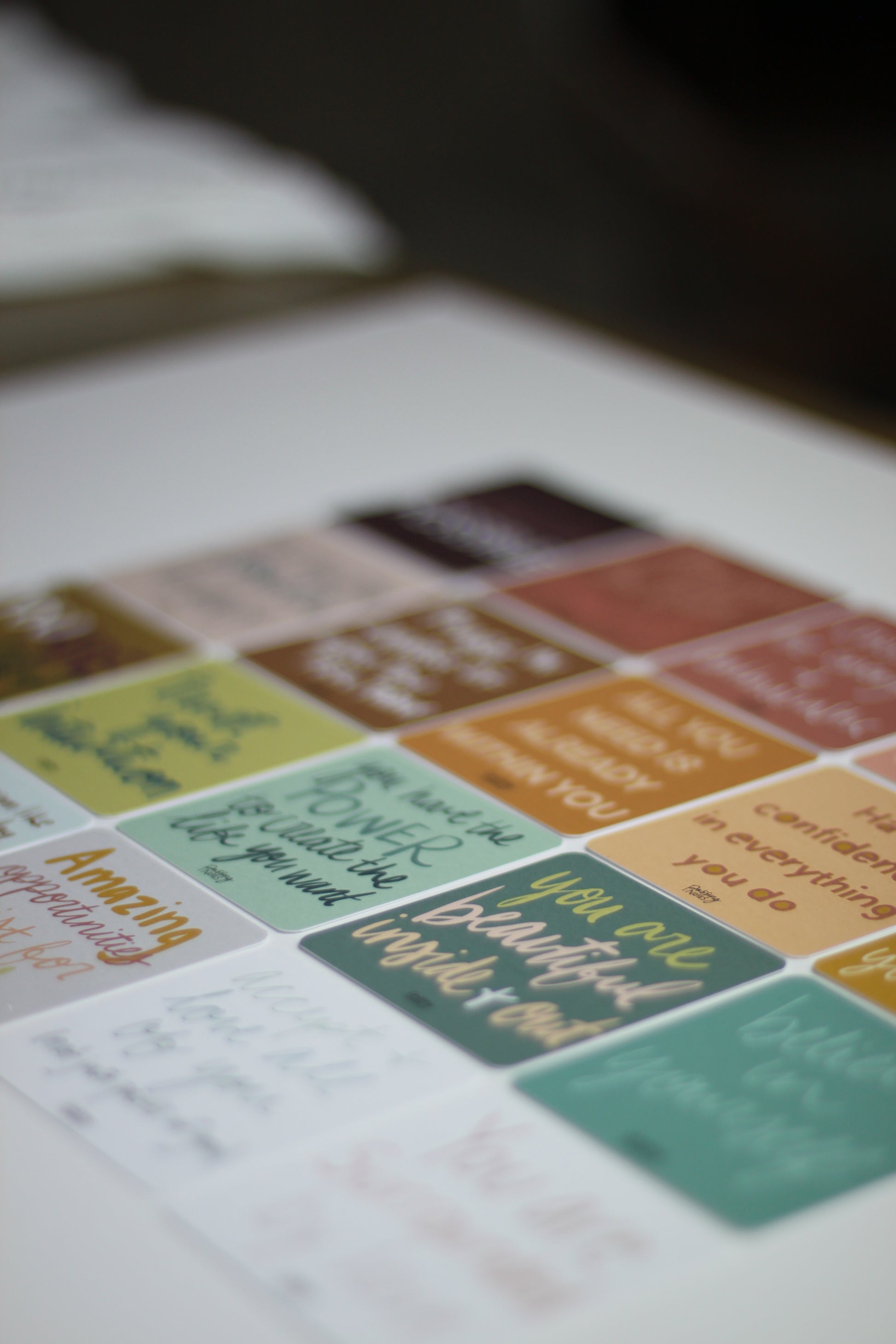 A close-up of colorful inspirational note cards with motivational quotes in various fonts. Arranged in neat rows, these vibrant note cards include shades of green, yellow, brown, and orange.