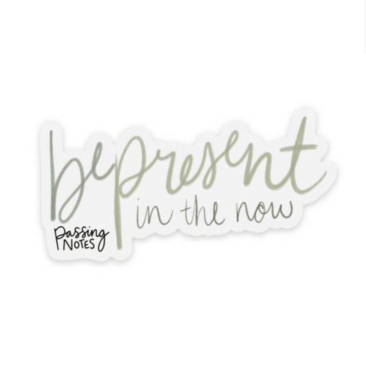 Clear backed sticker with handwritten green font that says "be present in the now"