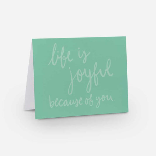 A2 horizontal sized card with a medium seafoam green background with a light seafoam green handwritten font that says "life is joyful because of you"