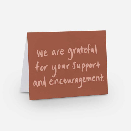 A2 horizontal sized card with a soft red background and light red handwritten font that says "we are grateful for your support and encouragement"