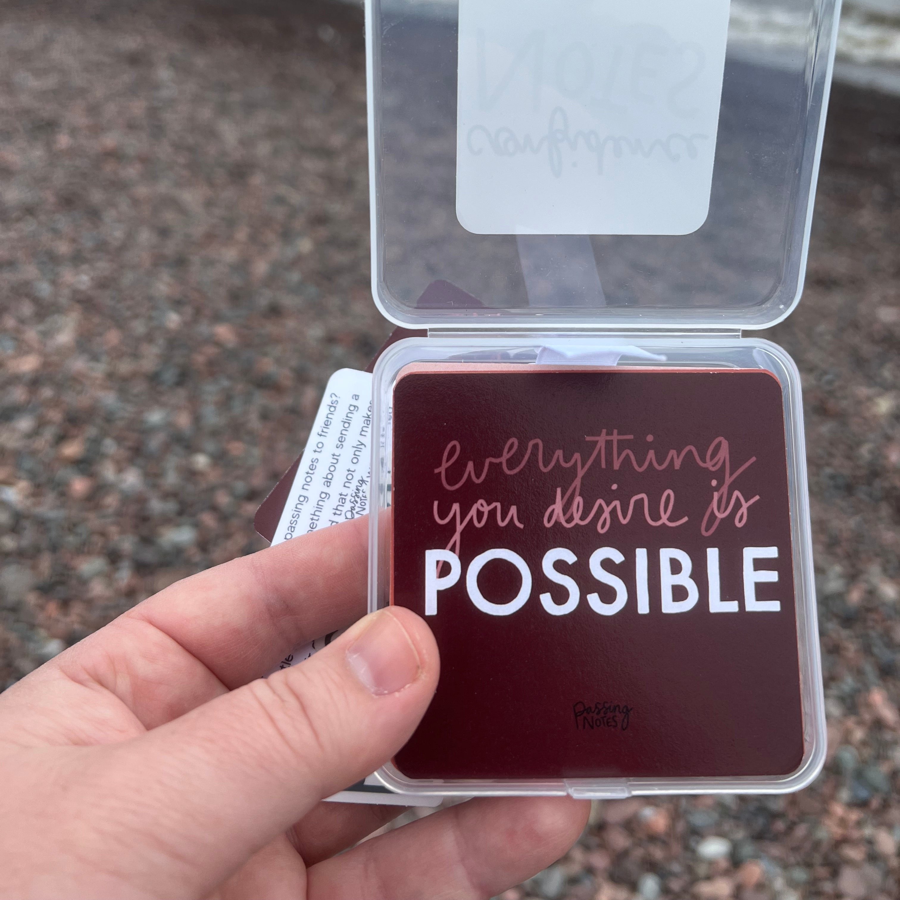 A person holding a small square card in a clear plastic case, reading "everything you desire is POSSIBLE" in white and pink text. The note card is included in a set of 40 encouraging notes to help you spread positivity and encouragement to others.