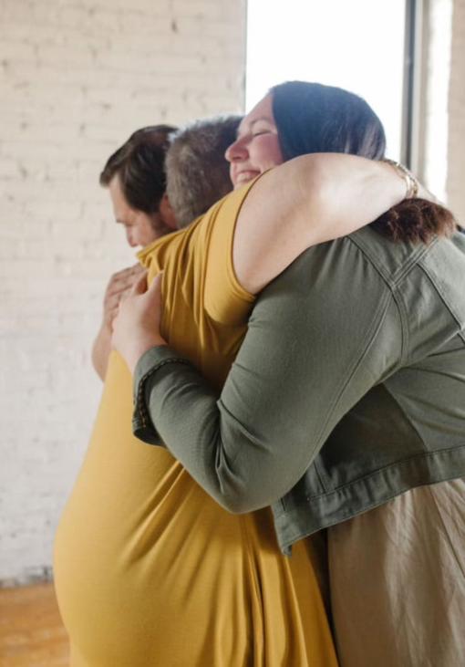 Two people hugging warmly in a bright room with a brick wall. One person is wearing a yellow shirt and the other a green jacket, exuding the kind of happiness you'd find on heartfelt greeting cards. They appear happy and content, capturing the essence of genuine connection.