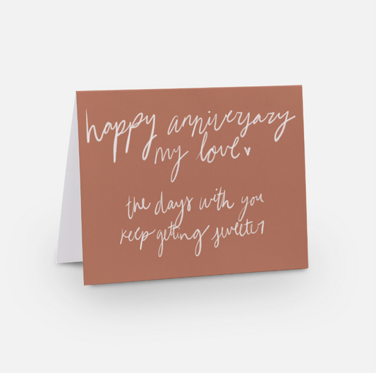 A2 sized horizontal card in a light red/peach color that says "happy anniversary my love the days with you keep getting sweeter" in a white handwritten font